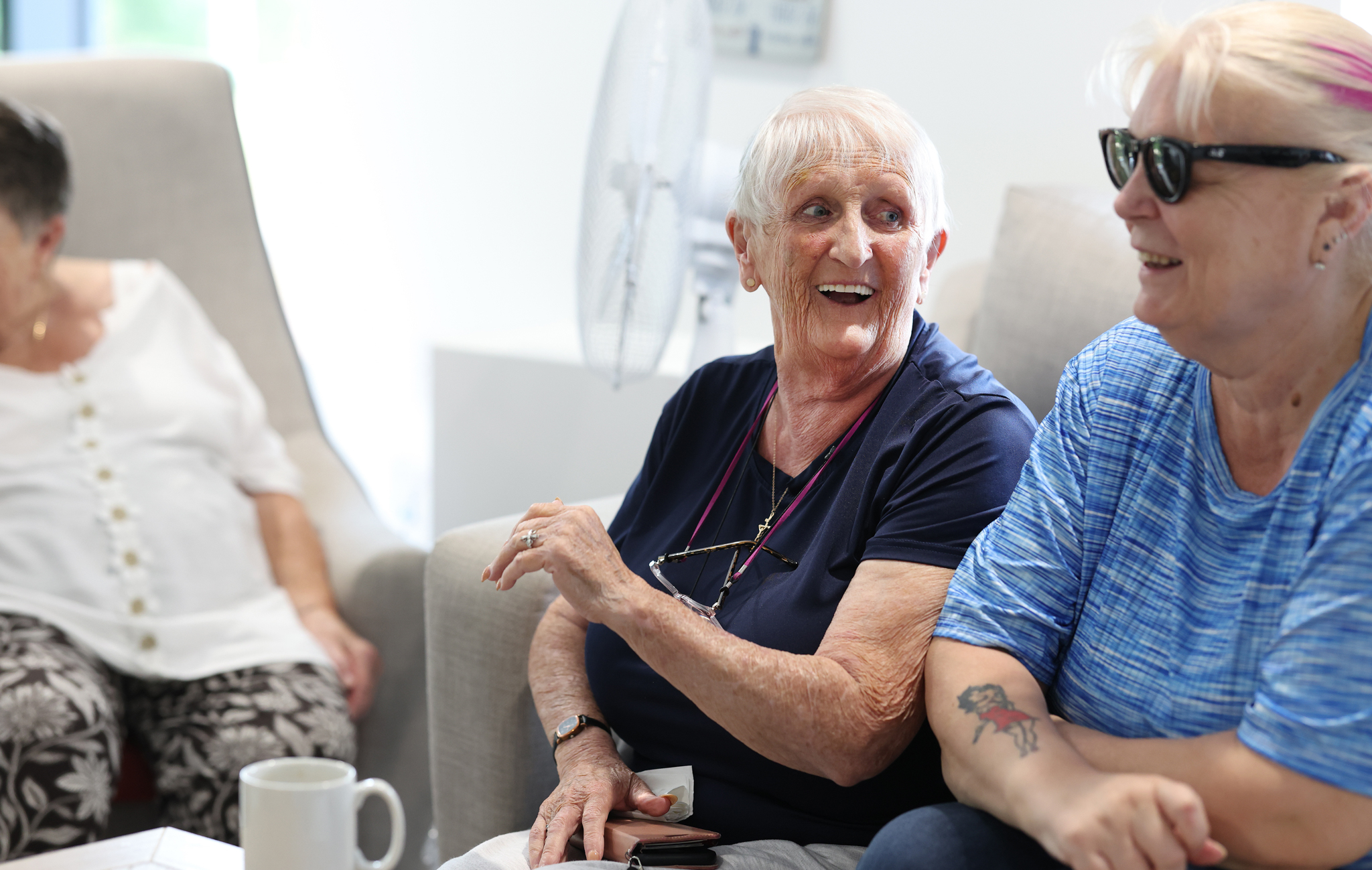 Three people sit together in a communal lounge, chatting and spending time together in a relaxed indoor setting.