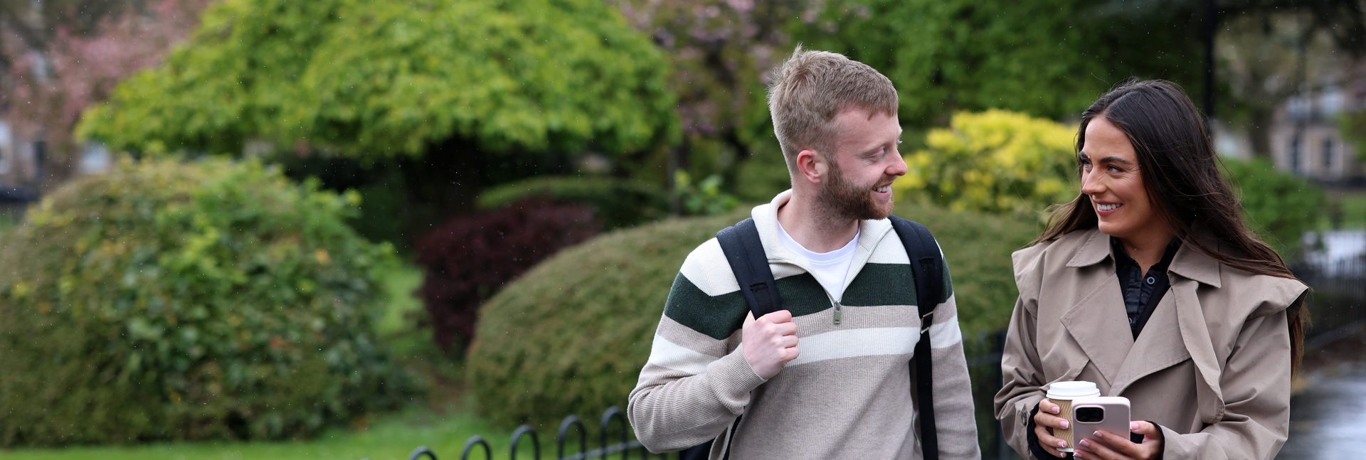 Two Magenta Living colleagues walking along a park path, looking at a phone together, with trees and greenery in the background.