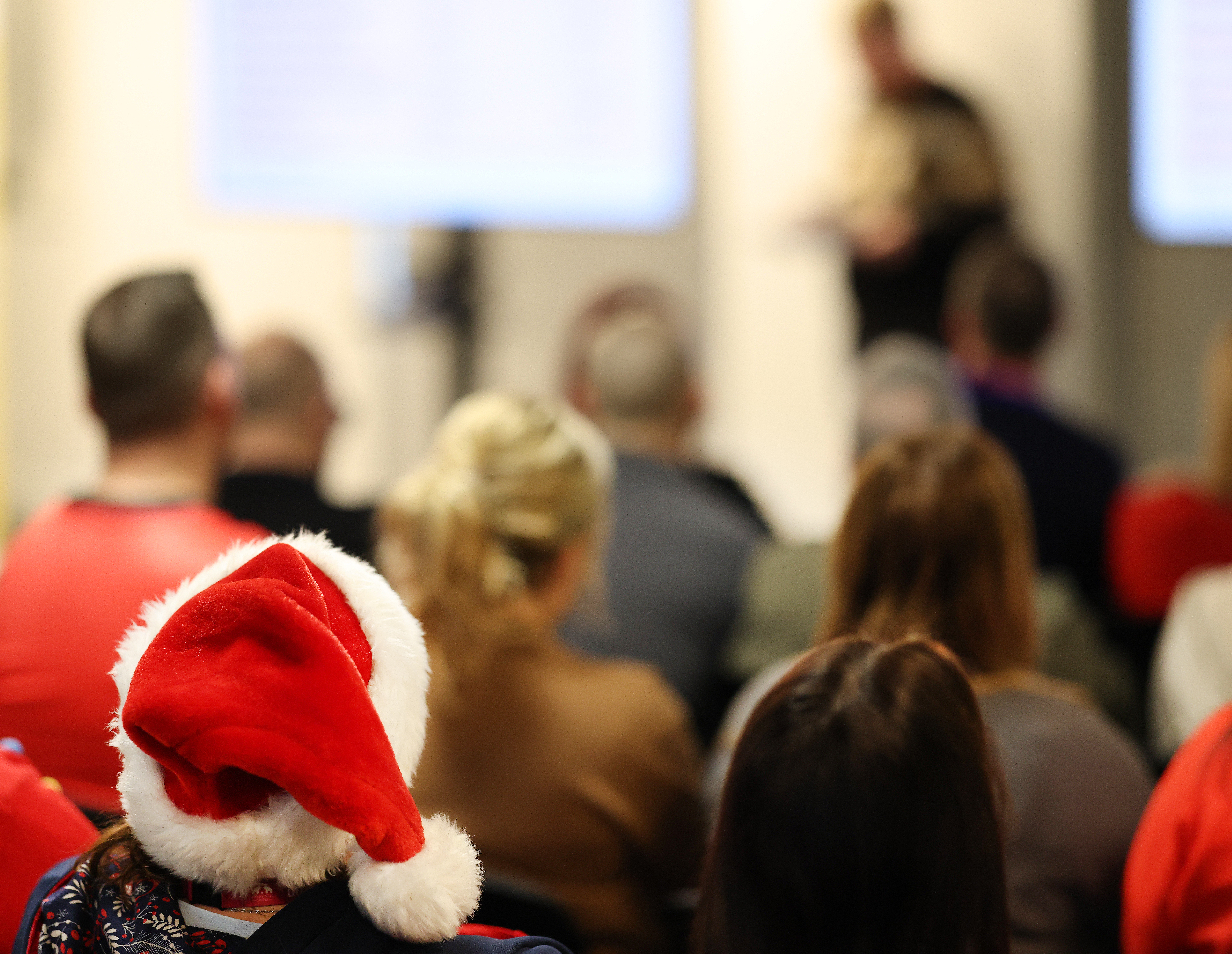 An audience watching a presentation, with one person wearing a Santa hat in the foreground.
