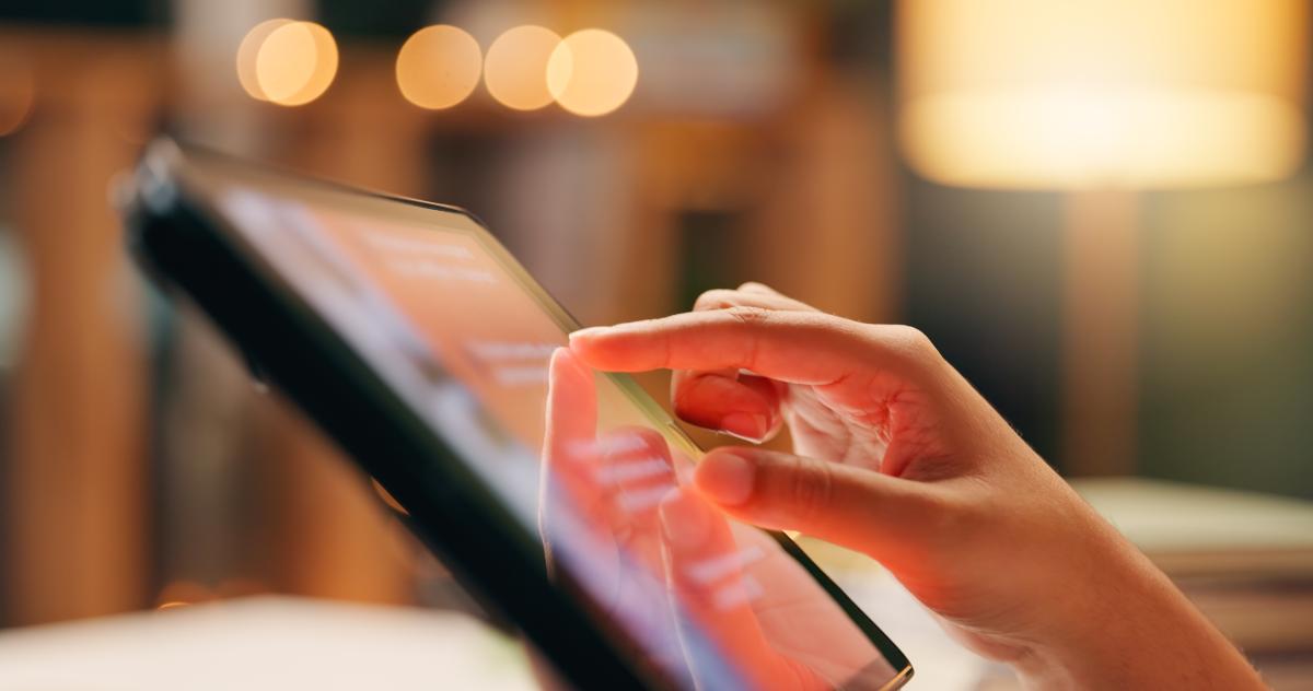Hand using a touchscreen tablet with warm indoor lighting.