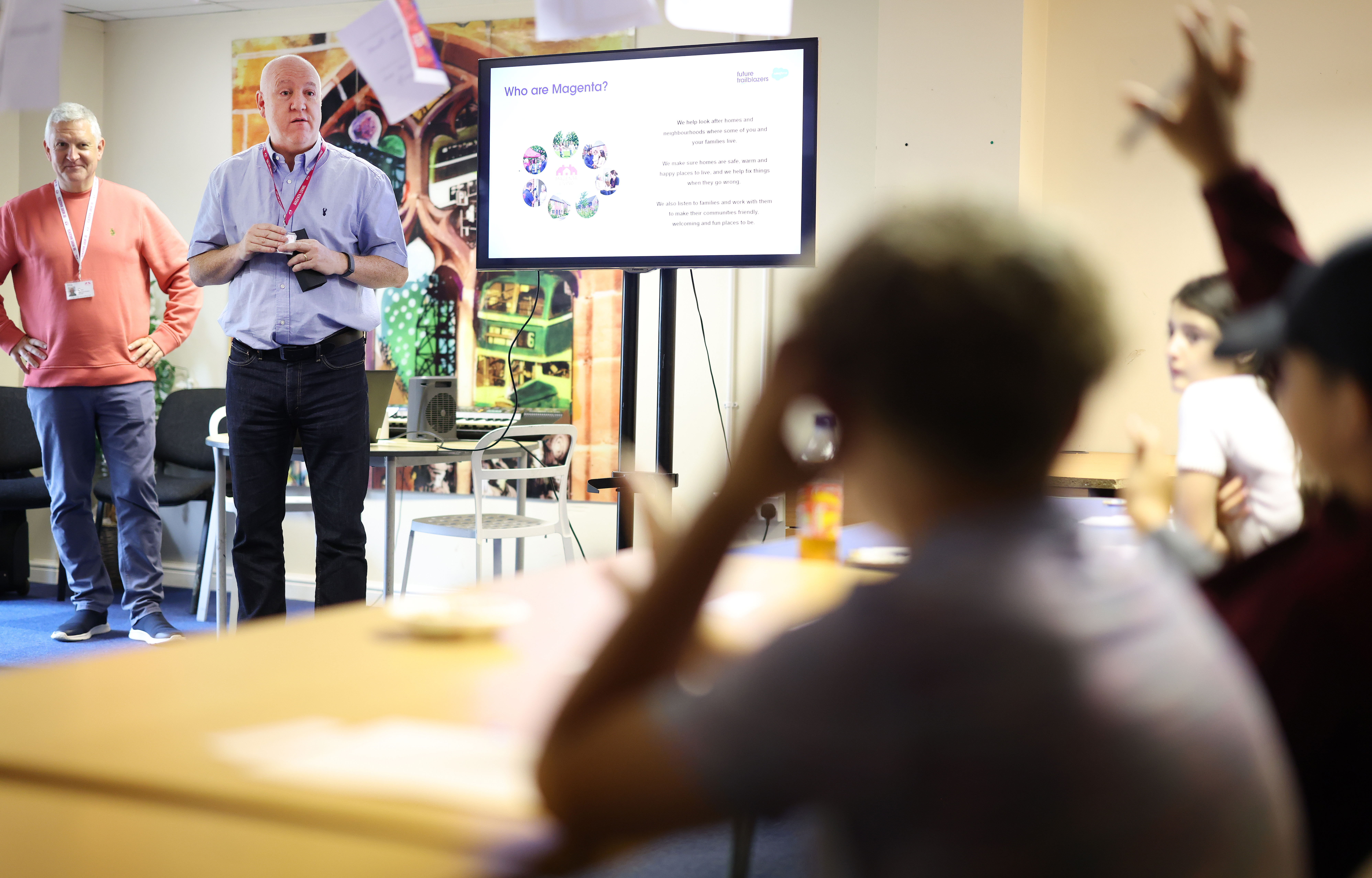 A presentation being delivered to a group of children and young people, with slides displayed on a screen at the front of the room.