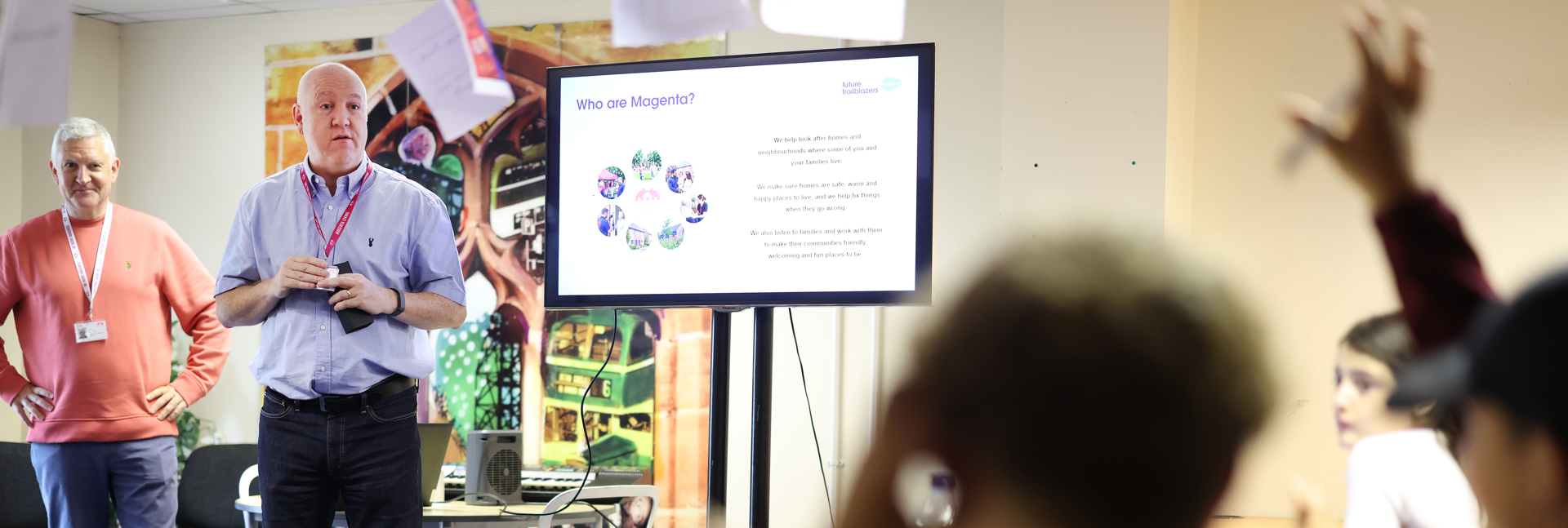 A presentation being delivered to a group of children and young people, with slides displayed on a screen at the front of the room.