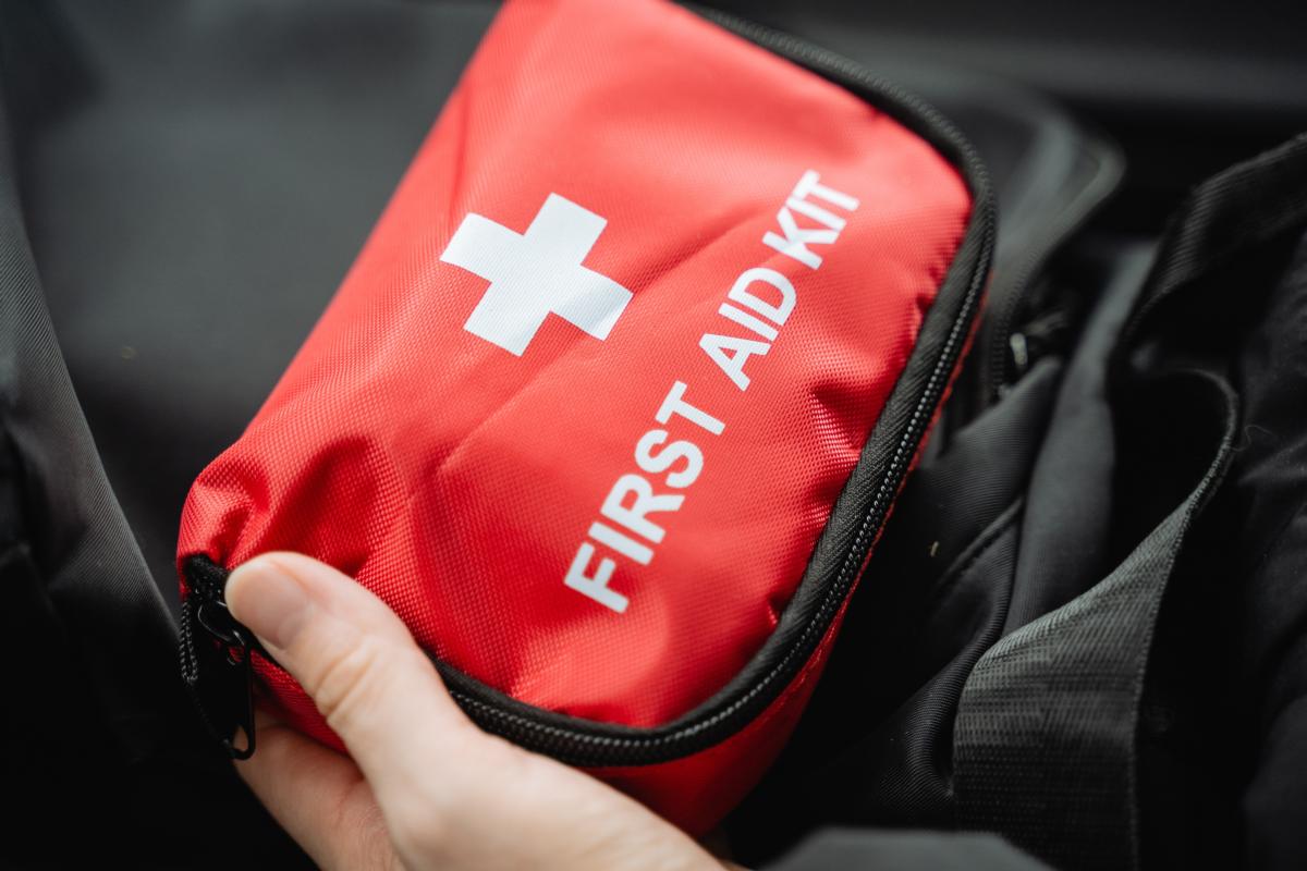 A hand holding a bright red first aid kit with a white cross on the front.