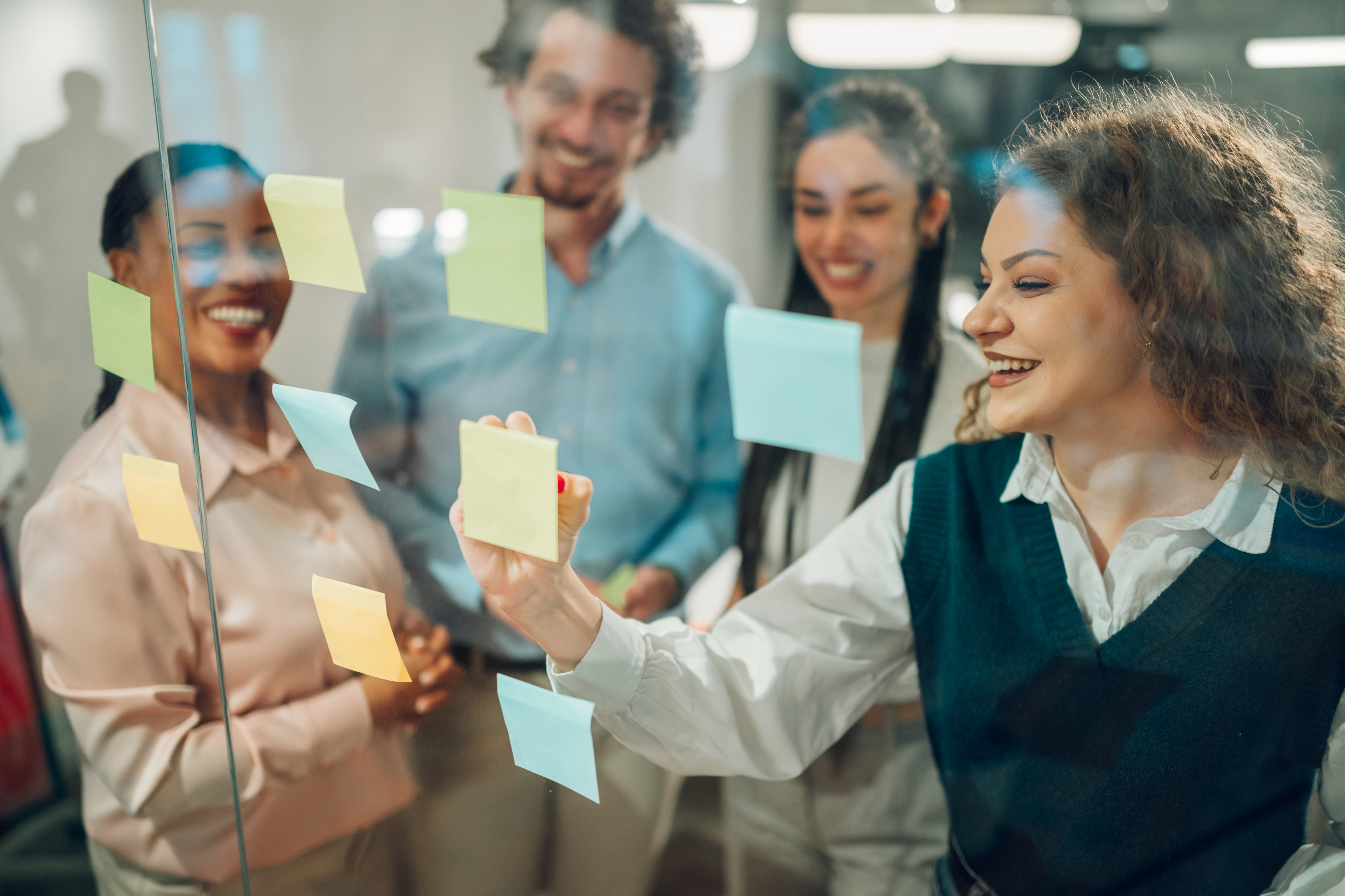 Group of colleagues working together using colourful sticky notes on a glass board