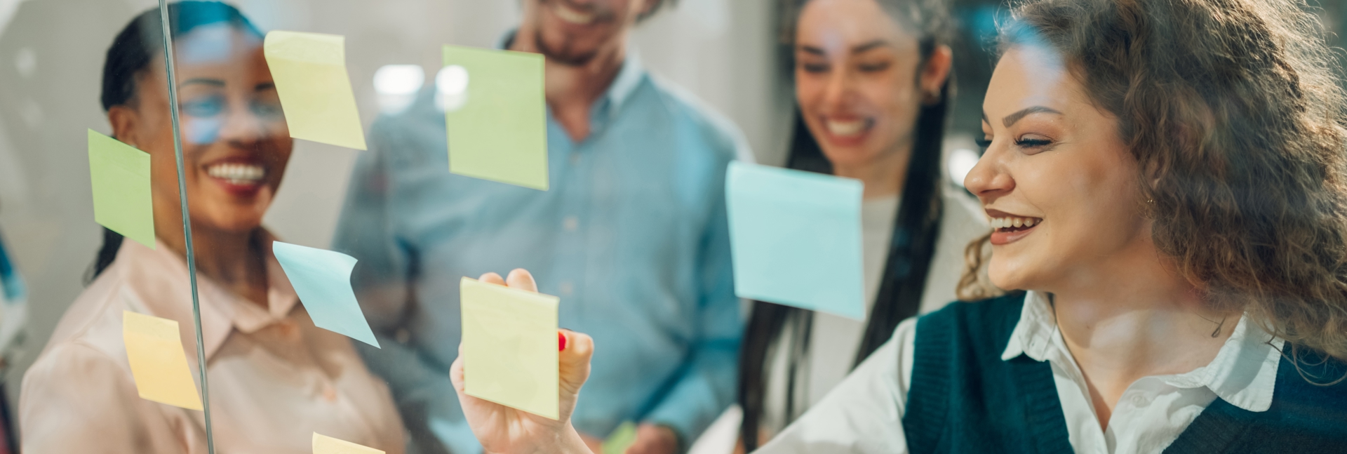 Group of colleagues working together using colourful sticky notes on a glass board