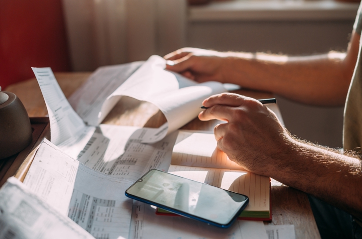 Hands sorting bills and documents on a desk with a mobile phone to the side.
