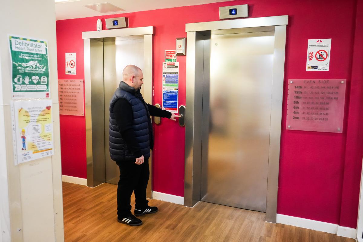 A person pressing the button for a lift in a brightly painted corridor with two lift doors.