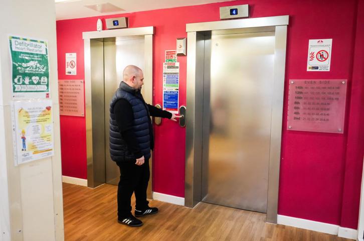 A person pressing the button for a lift in a brightly painted corridor with two lift doors.