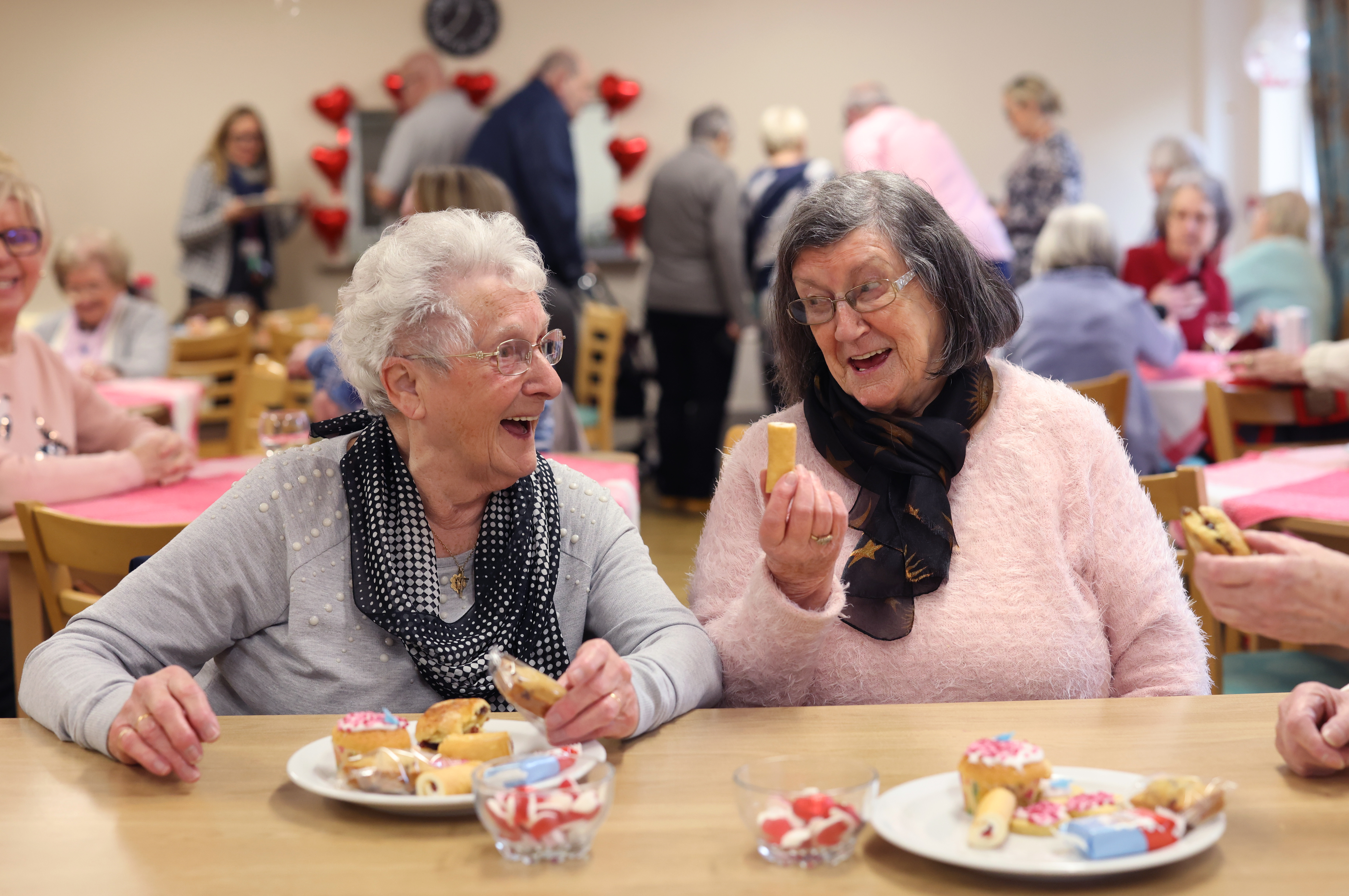 A busy community room with people chatting and sharing refreshments.