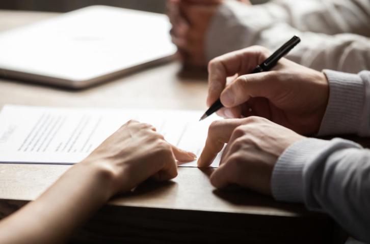 Person signing a document while someone points to the section to complete.