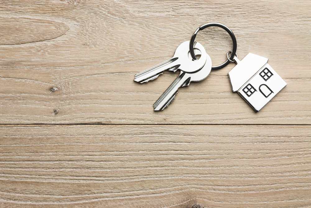 House keys with a house-shaped keyring on a wooden surface.