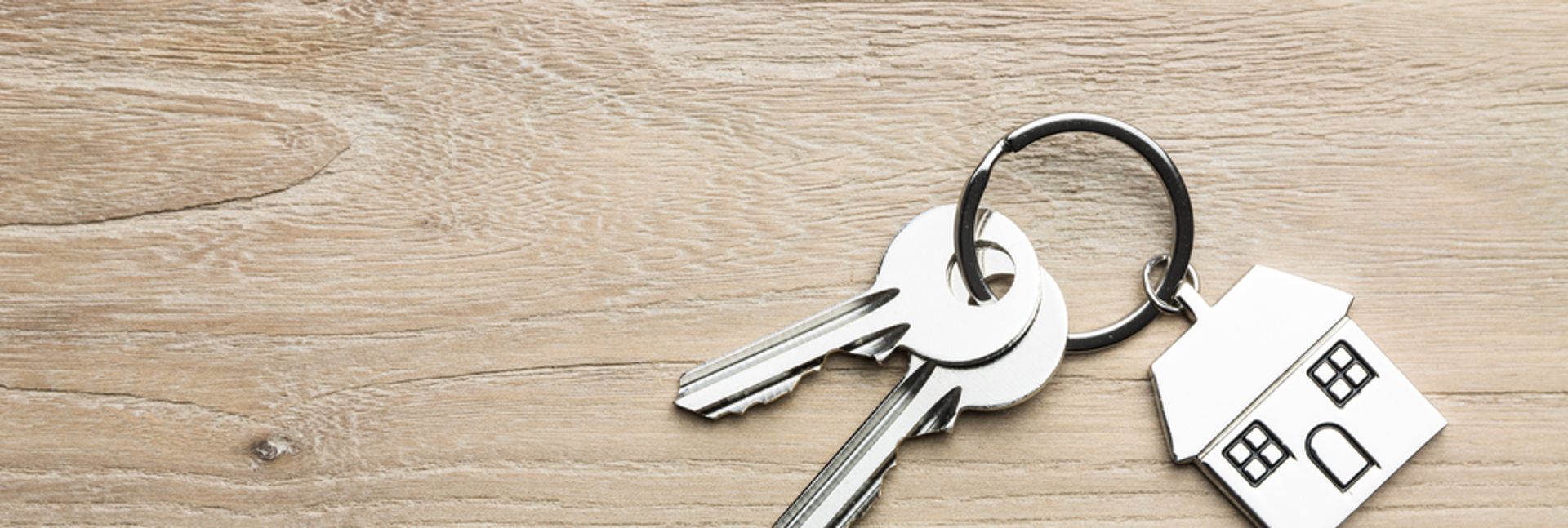 House keys with a house-shaped keyring on a wooden surface.