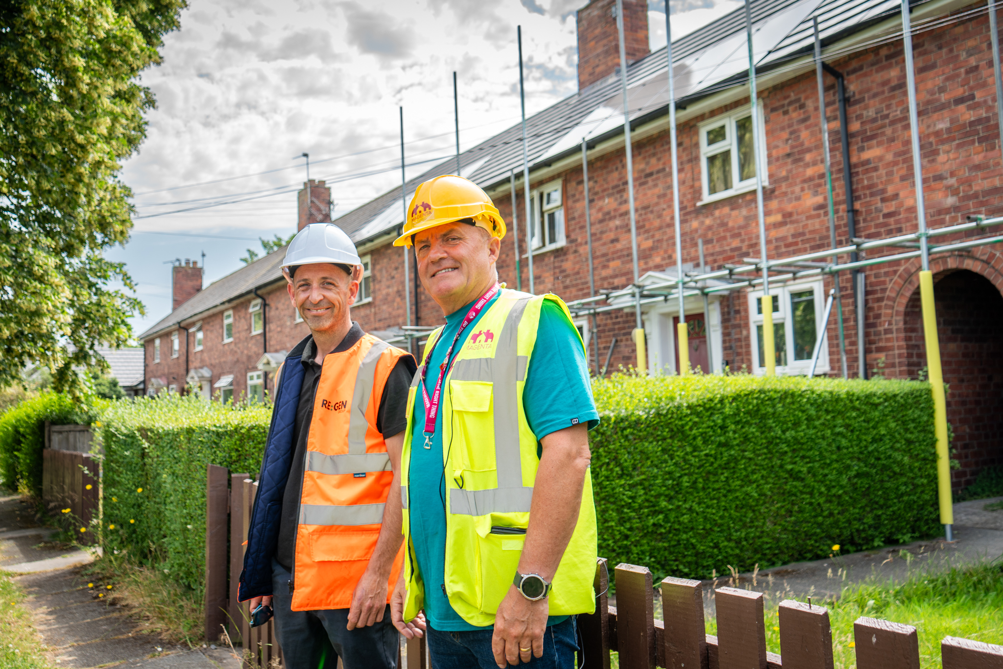 Two people in safety gear standing outside homes with rooftop solar panels.