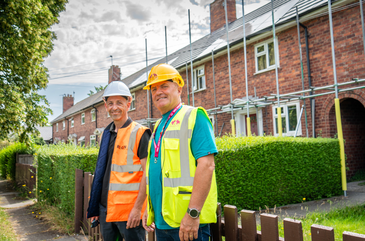 Two people in safety gear standing outside homes with rooftop solar panels.