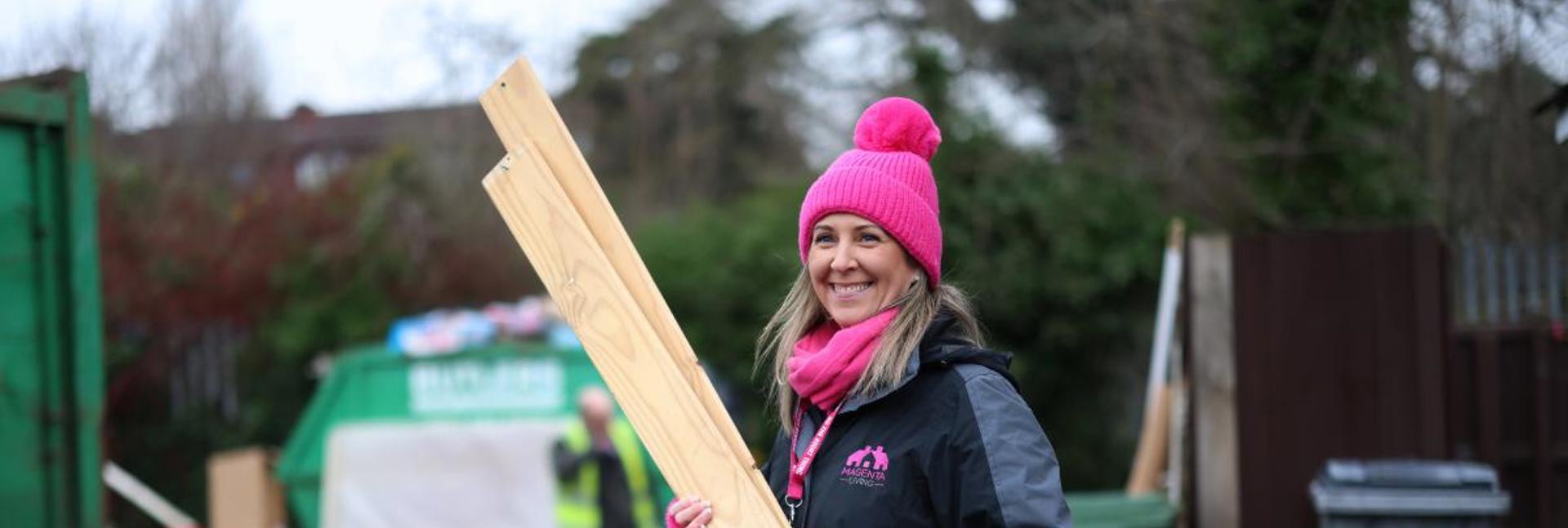 A person taking part in a community clean‑up, holding long wooden boards on a street with waste being cleared in the background.