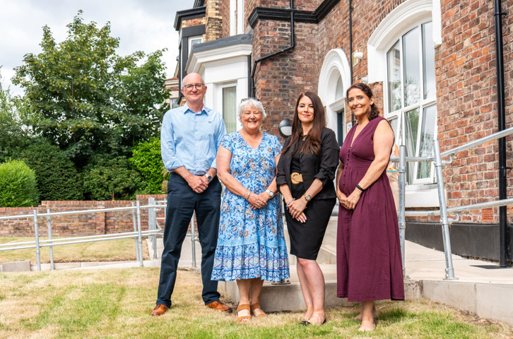 Four people standing together outside a brick building.